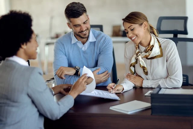 Three people at a desk and one of them signing a document